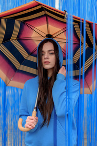 年轻美丽的女人与橙色的雨伞时髦摆在蓝色背景。雨概念