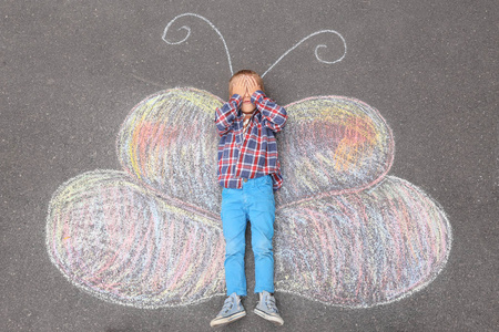 小男孩躺在粉笔画蝴蝶户外