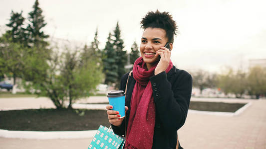 有吸引力的混合种族商业妇女谈论智能手机和喝咖啡走在城市街道购物袋
