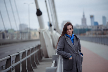 穿着大衣的年轻女子, 在刮风的天气里走在城市的桥上。城市秋天冬天样式
