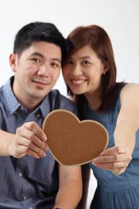 一对夫妇站在一起抱着一颗心形的纸板