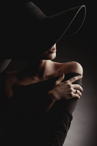 深色工作室肖像的优雅的女人在黑色宽帽和黑色礼服。隐藏的半边脸