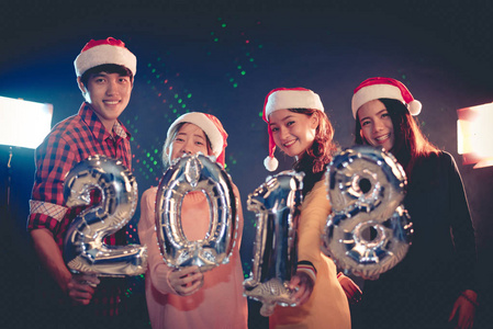 亚洲人谁戴圣诞帽庆祝新年党2018和显示字母表气球在夜间酒吧或酒吧。圣诞节和新年2018概念。夜生活中的圣诞派对
