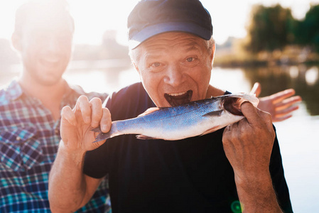 一个穿着黑色 t恤的老人在拿着鱼的时候摆姿势。他假装想吃她
