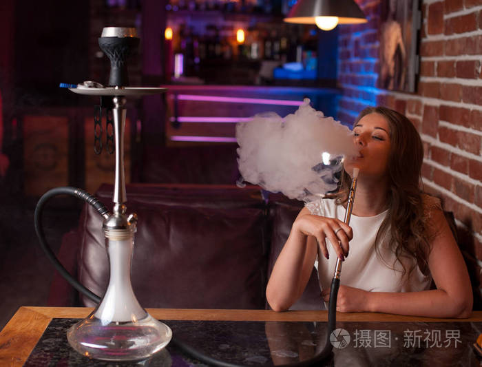 美丽的女孩在一件白色衬衫抽烟在酒吧里面的水烟