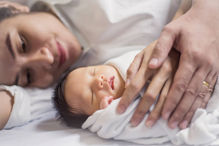 年轻的亚裔父母躺在床上抱着新生婴儿