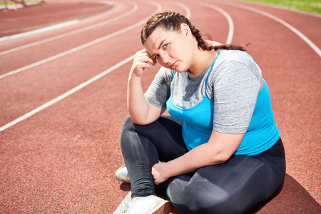 抑郁症年轻丰满的女性坐在体育场后训练