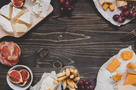 奶酪选择与水果和小吃的木制深色表与复制空间。顶部视图背景