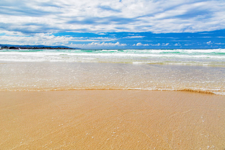 在海滩上留下的波浪。水通过沙子出现, 在距离绿色海水。一个水平的镜头, 蓝天与风景如画的云彩
