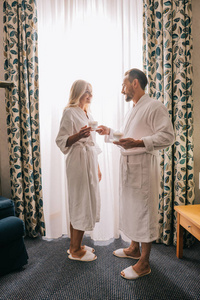 幸福成熟情侣的全长观浴袍喝咖啡, 在酒店房间里互相微笑