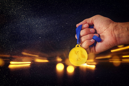 男子手持金牌的黑色背景与闪光的覆盖。奖和胜利概念