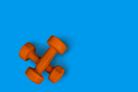 橙色健身哑铃上的蓝色背景, 运动设备的顶部视图。健康理念