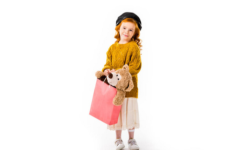 红色头发孩子藏品泰迪熊在购物袋隔绝在白色