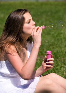 年轻女孩在夏天绿色公园吹肥皂泡泡