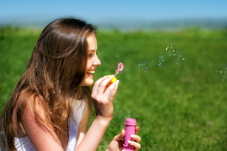 年轻女孩在夏天绿色公园吹肥皂泡泡