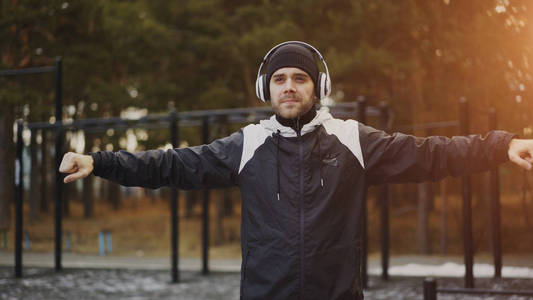 英俊的人在耳机做热身运动, 当听音乐在冬天公园