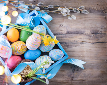 复活节五颜六色的彩蛋与春天的花朵和蓝色缎带在木桌上