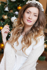 美丽的年轻女子穿着白色套衫坐在木地板在家里与装饰圣诞树背景