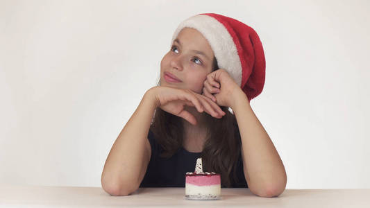 美丽的少女在圣诞老人的帽子坐在白色的背景下许愿