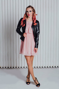 美丽的年轻女子与明亮的化妆和粉红色的头发在皮夹克和粉红色的礼服摆在工作室
