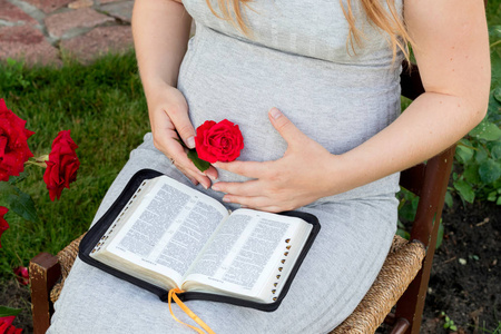 怀孕妇女读书书 (圣经) 在庭院里.怀孕, 新生活, 为人父母的观念.