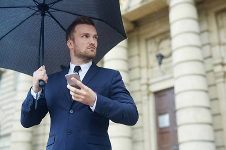 企业领导者用智能手机在雨天等待某人