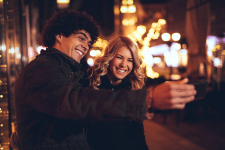 年轻美丽欢快的情侣采取自拍在城市街道在除夕夜与许多灯背景
