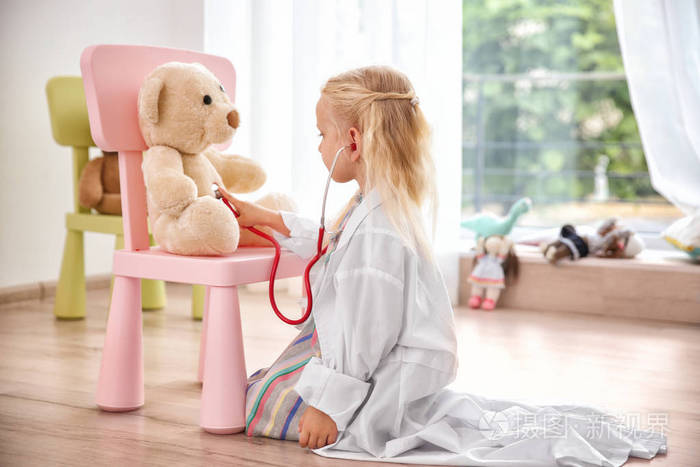 小女孩在地板上玩玩具熊和听诊器的医疗外套