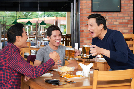 兴奋的成熟的越南男子带啤酒到他的朋友的桌子