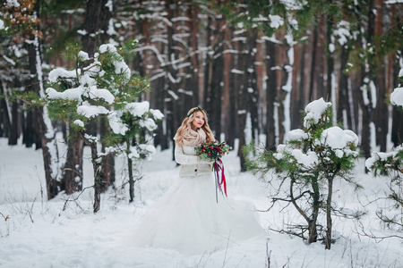 年轻的新娘在白雪皑皑的森林里摆着花束。冬季婚礼。艺术品