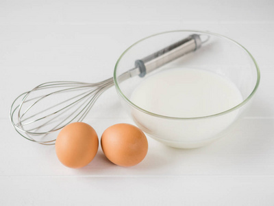 两个鸡蛋, 一个扫和一碗牛奶在白色的木桌上