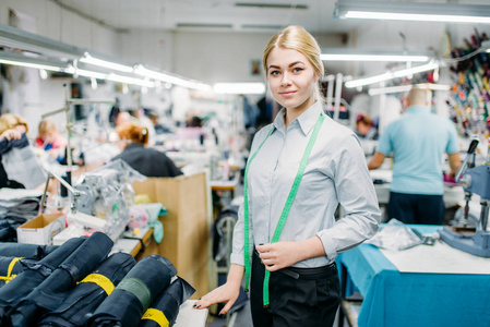 漂亮的年轻女裁缝在工作场所, 缝纫材料在桌子上。成衣厂的裁缝或成衣