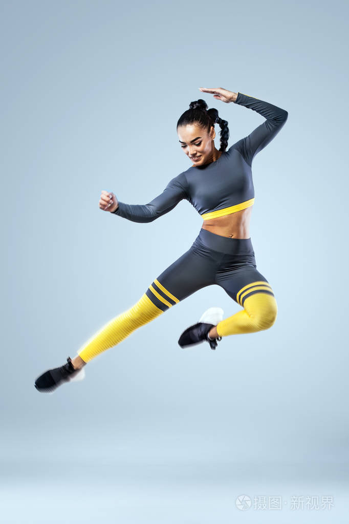 迷人的兴奋健身女孩舞者在运动跳跃的喜悦孤立的灰色背景