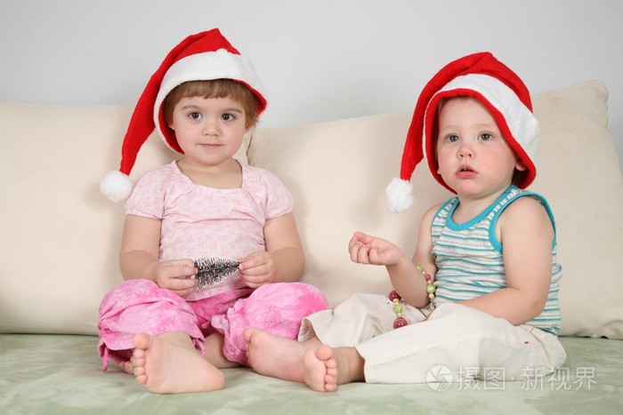 两个孩子在沙发上戴着圣诞帽