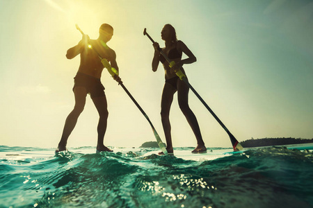 日落时分 Paddleboarding。年轻夫妇在海与桨和板