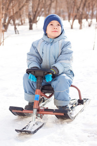 快乐的小男孩在冬天的公园里散步，在雪橇上滑行