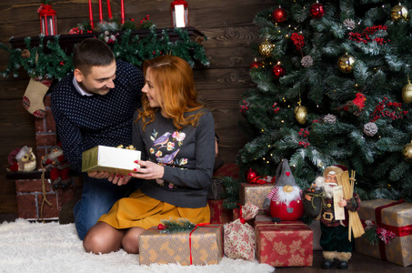 亲友互赠快乐的年轻人在圣诞树旁的壁炉旁互赠礼物.圣诞快乐照片