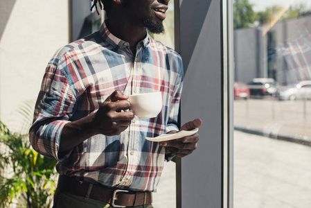 非洲裔美国人在窗口站立时喝咖啡的裁剪视图