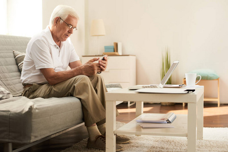 现代老人的肖像学习使用智能手机和笔记本电脑在家中舒适的客厅