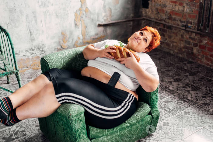 肥胖妇女坐在扶手椅上吃三明治不健康的生活方式和减肥观念