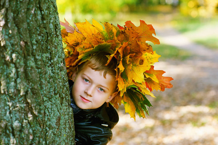 漂亮的男孩在公园里用树叶在她头上的花环的秋天肖像照片