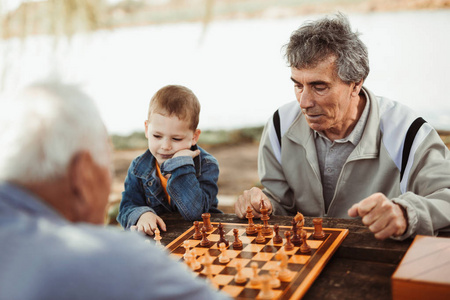 活跃的退休老人在公园里玩象棋, 花时间陪小孙子