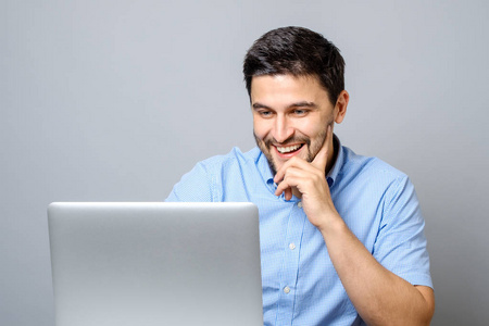 年轻的微笑的人坐在办公桌上的笔记本电脑的肖像