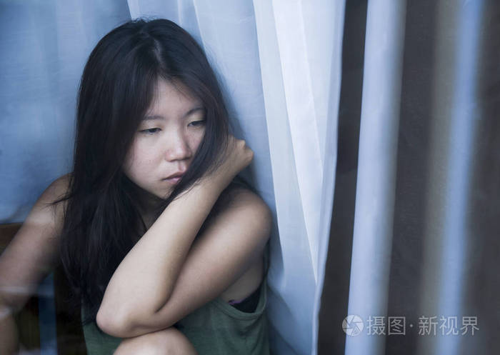 年轻的忧郁和忧郁的亚裔中国女性看着窗外的沉思悲伤的