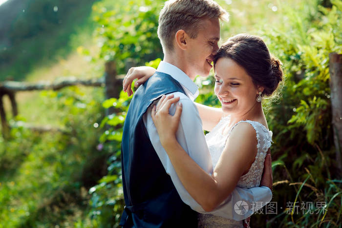 美丽的新婚夫妇的情感肖像可爱的微笑温柔地拥抱在阳光明媚的绿色花园