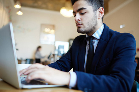 严重的年轻商人在咖啡馆里打字的笔记本电脑键盘