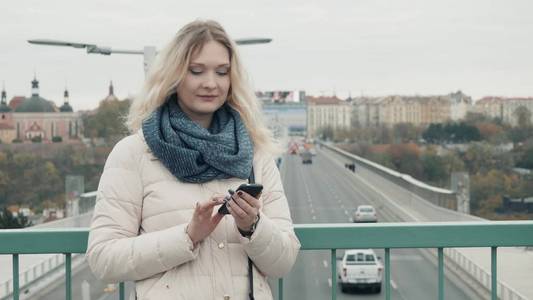有吸引力的游客穿着休闲装在智能手机上的应用在城市的导航, 时髦的女孩站在市区设置促销背景通过手机发短信