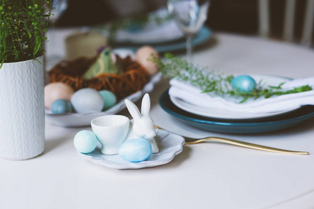 北欧斯堪的纳维亚风格的复活节和春季节日餐桌, 用蓝色和白色的自然色调装饰着鸡蛋兔子鲜花和蜡烛