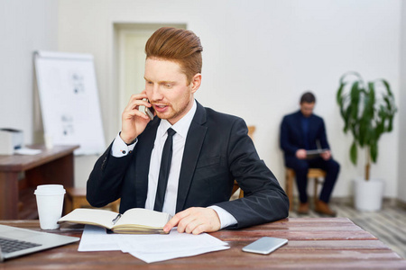 年轻的红头发的男子在办公室接听电话的职业套装的肖像