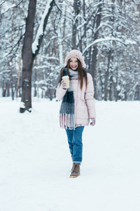 冬季穿咖啡的迷人女人在公园里走